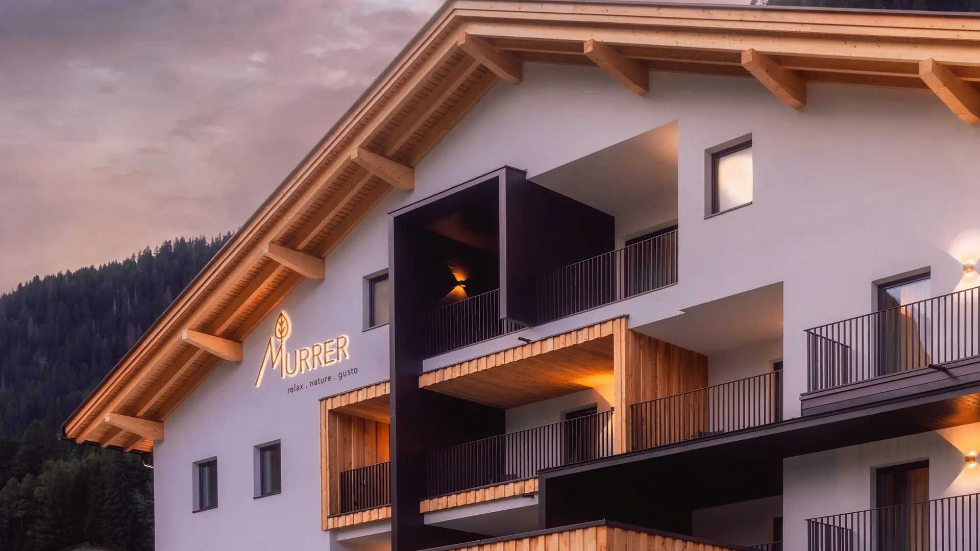Facciata dell hotel al crepuscolo con rivestimento in larice davanti al pendio boscoso